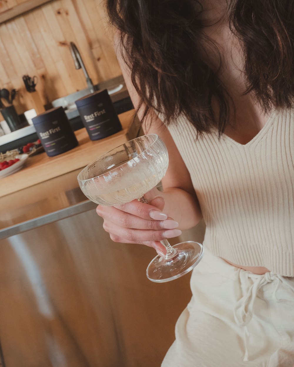 A hand holding a coupe glass of the drink in a kitchen.