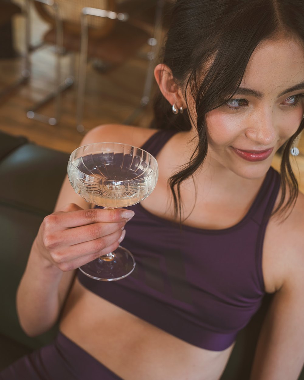 A woman smiling and holding up a coupe glass.